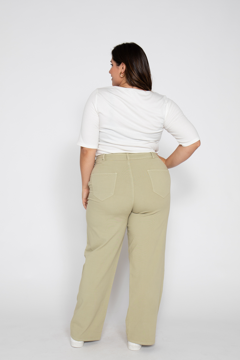 Plus-size woman shows back view of high-waisted flare pants, standing with casual pose, wearing a white top.