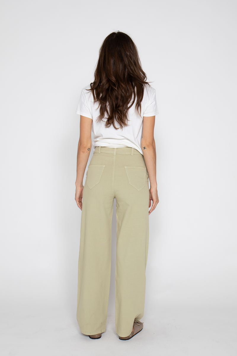 Woman shows back view of lightweight high-waisted flare pants, facing away, in sandals and a white t-shirt.