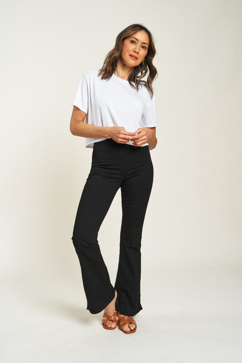 Flare pull-on pants in black, model facing forward with hands in pockets, showing relaxed fit and wide hem.
