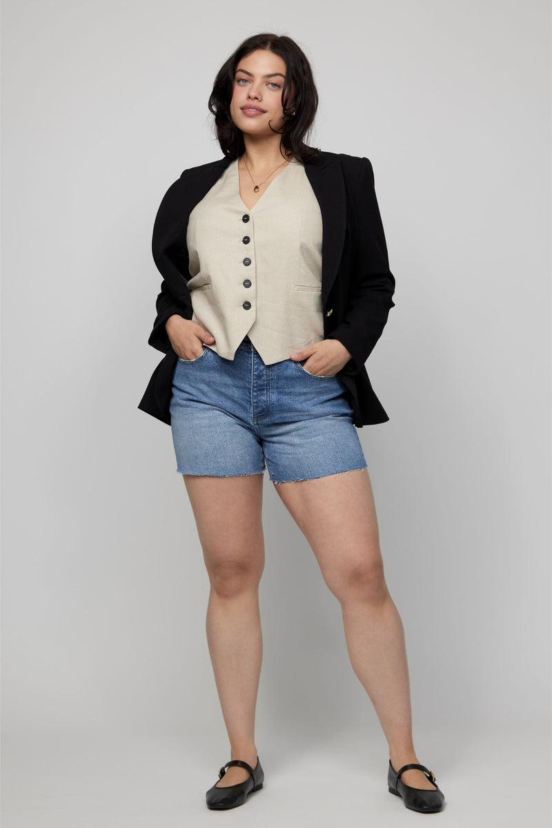 Plus-size model wearing high-rise denim shorts and a black blazer with a beige vest for a tailored casual look.