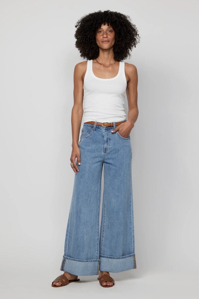 Woman wearing mid-rise wide-leg cuffed jeans in light blue denim, styled with a white tank top.