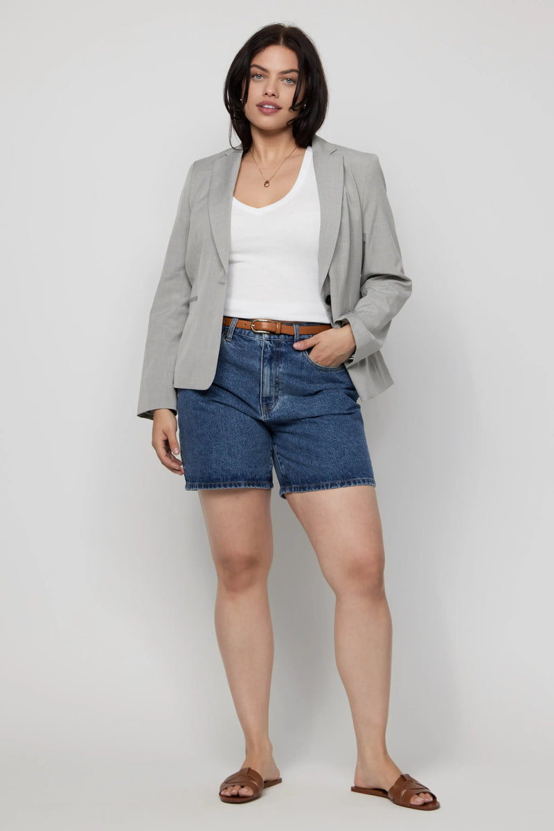 Plus-size model wearing high-rise dark wash denim shorts with a grey blazer and white tee.