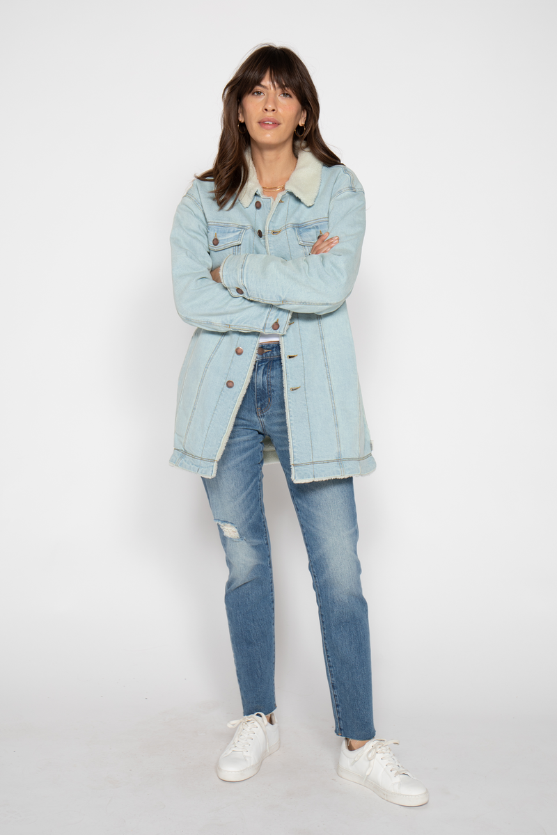 Front view of a model wearing a light blue sherpa-lined coat with button details, paired with jeans and white sneakers for a relaxed look.