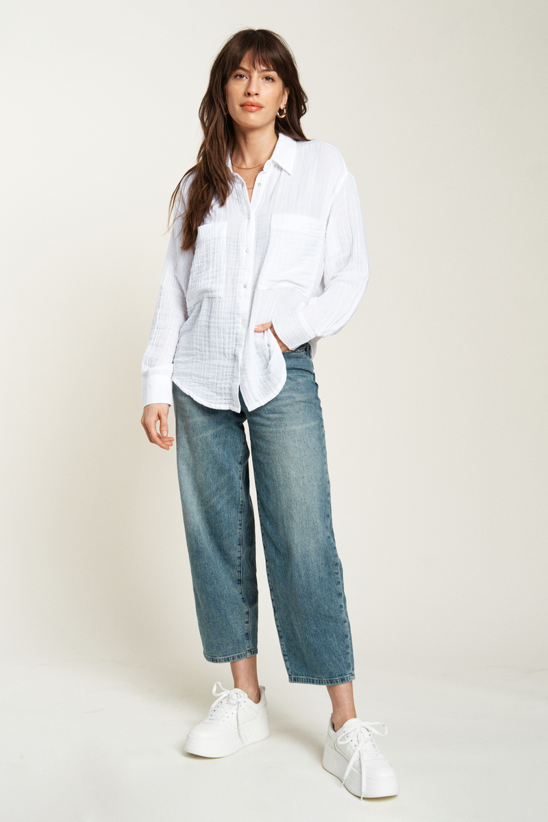 White lightweight button-up top featuring a relaxed fit and long sleeves, paired with light-wash jeans for a casual look.
