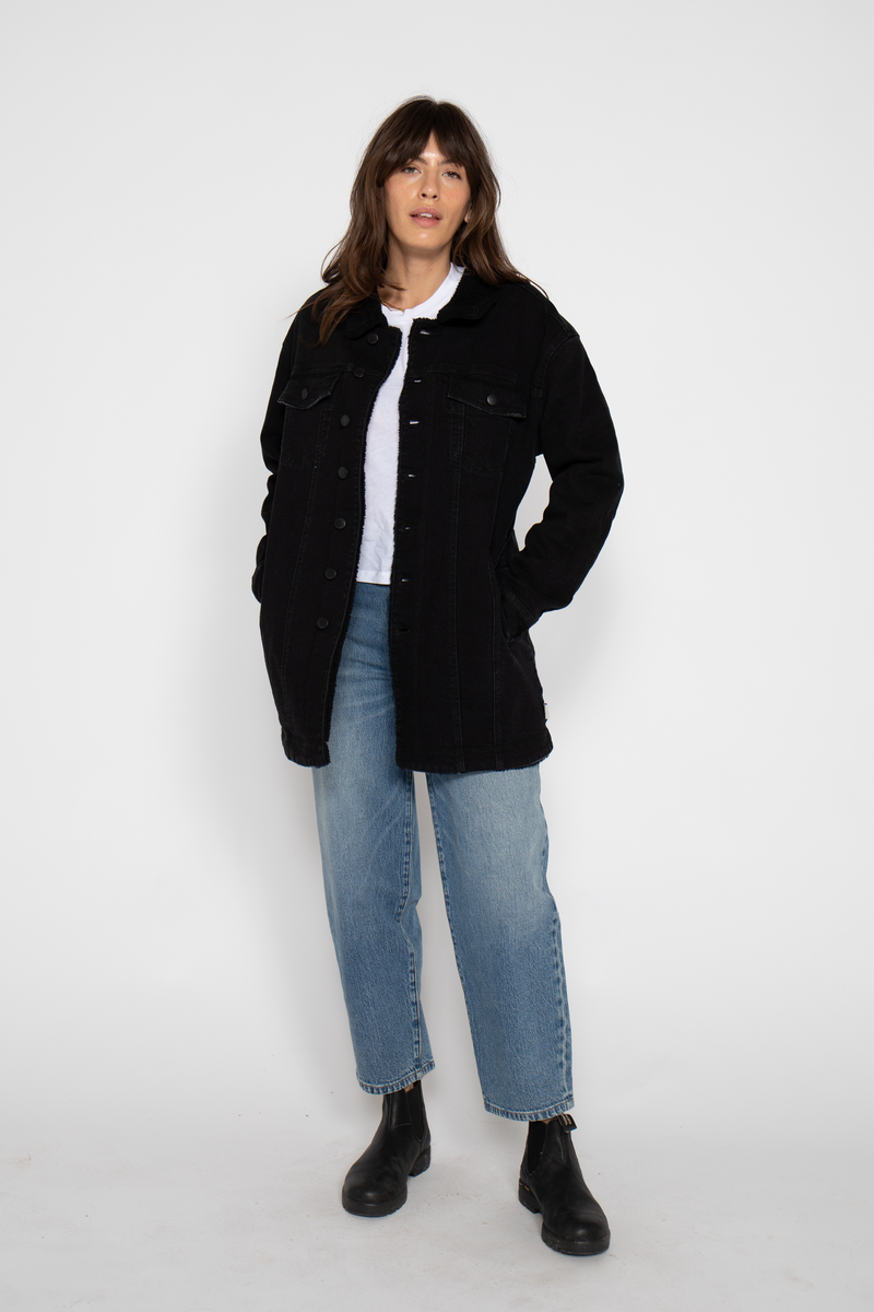 Front view of a model wearing a black sherpa-lined coat, styled with a white top, blue jeans, and black boots.