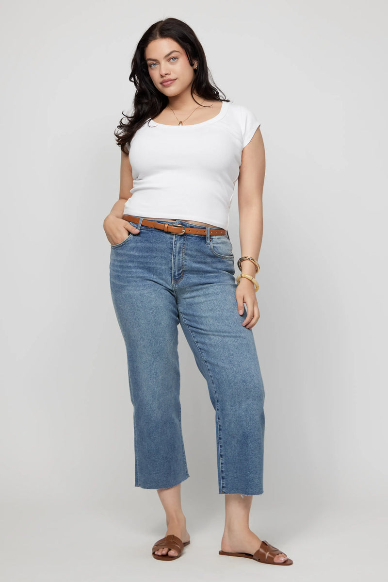 Plus-size woman in cropped denim jeans and a white tee, styled casually with sandals and gold accessories.