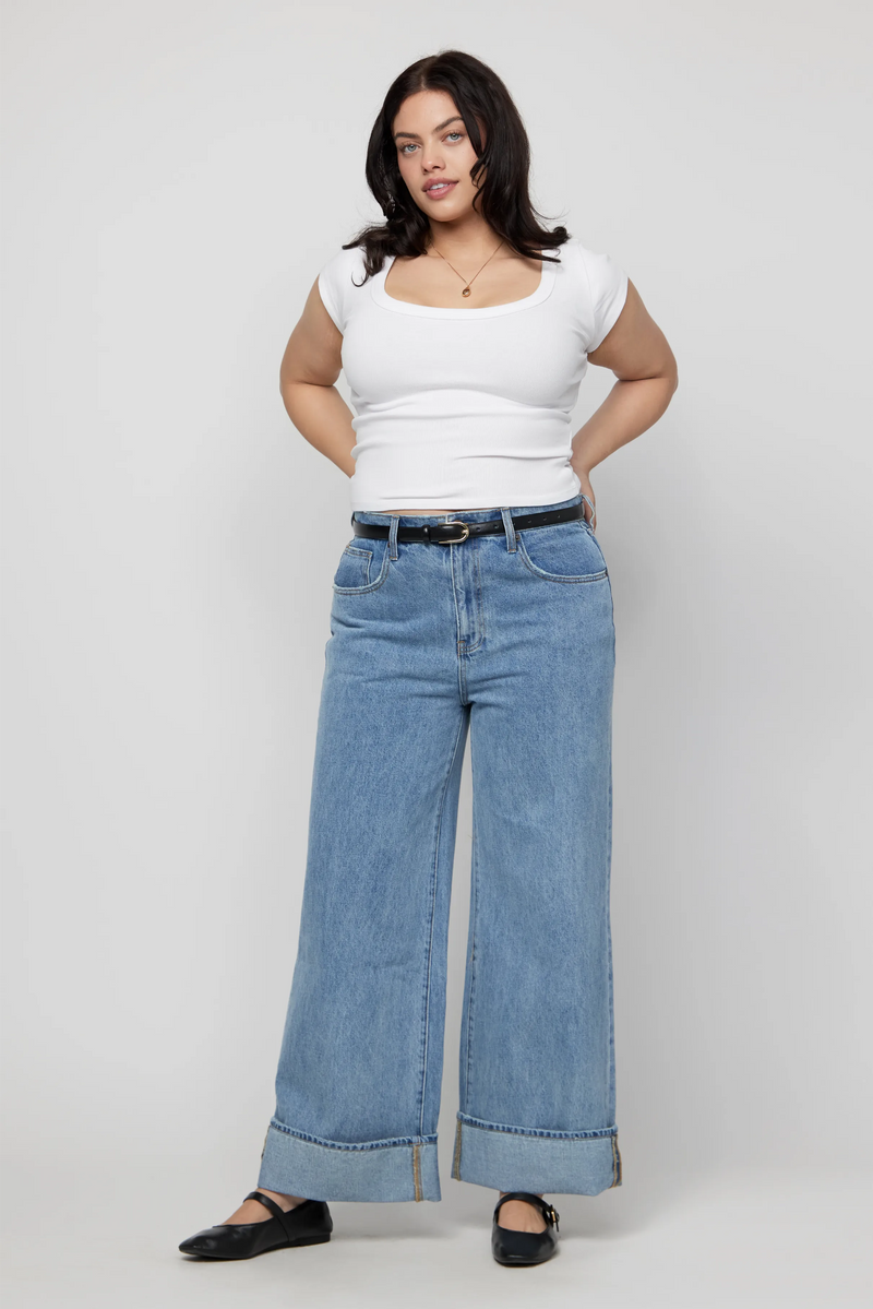 Plus-size woman wearing mid-rise wide-leg cuffed jeans in light denim with a white tee.