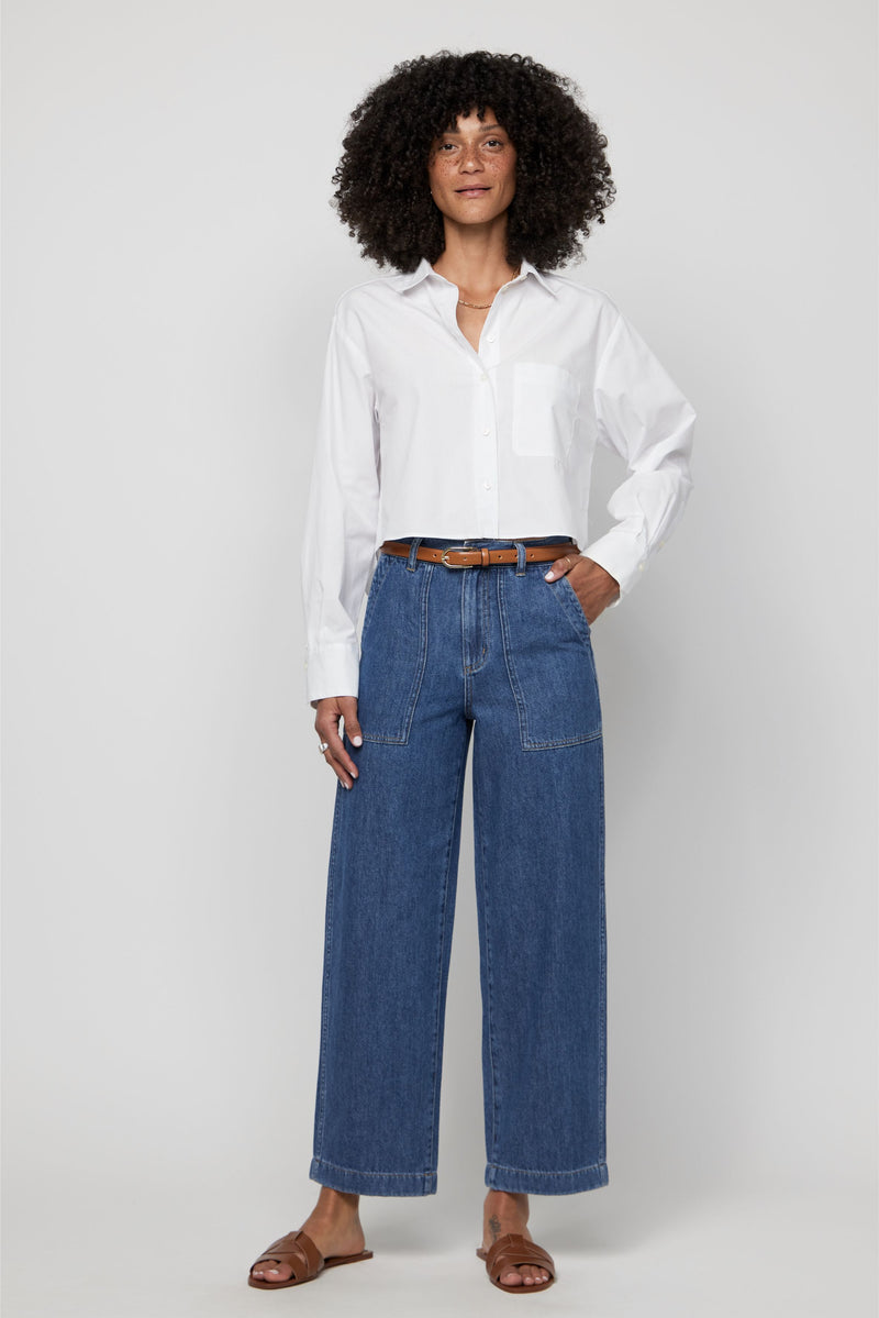 Woman wearing high-rise wide-leg cropped denim trousers in medium blue wash with a white button-up shirt.