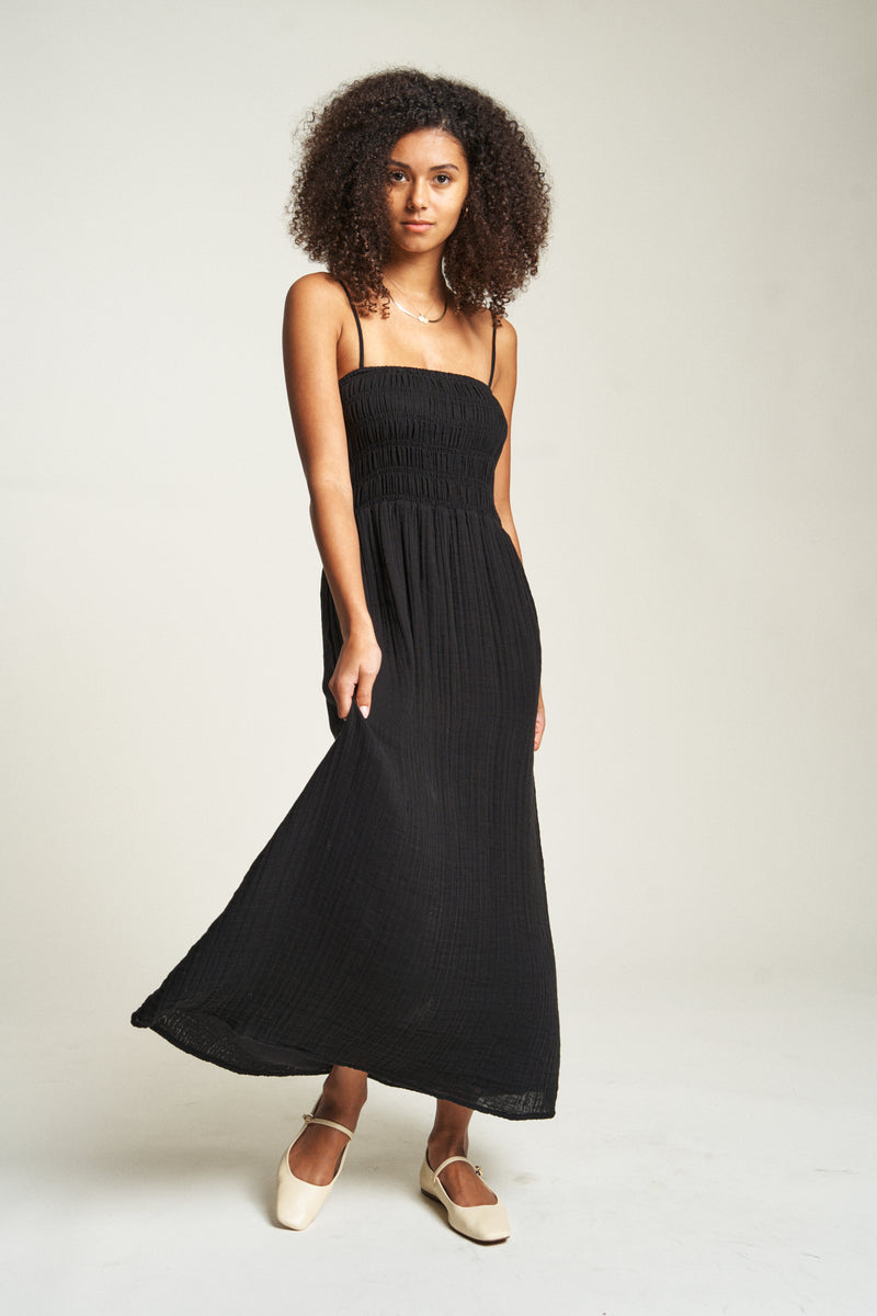 Flowy black cotton maxi dress with a smocked bodice, offering a sleek and stylish look for warm summer days.