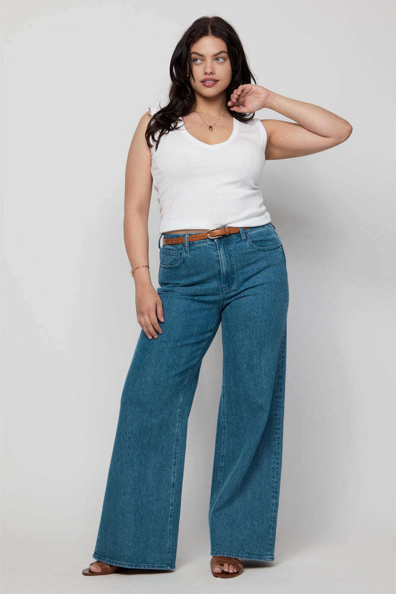 Plus-size model wearing high-rise wide-leg jeans in medium indigo wash with a white tank, styled for everyday comfort.