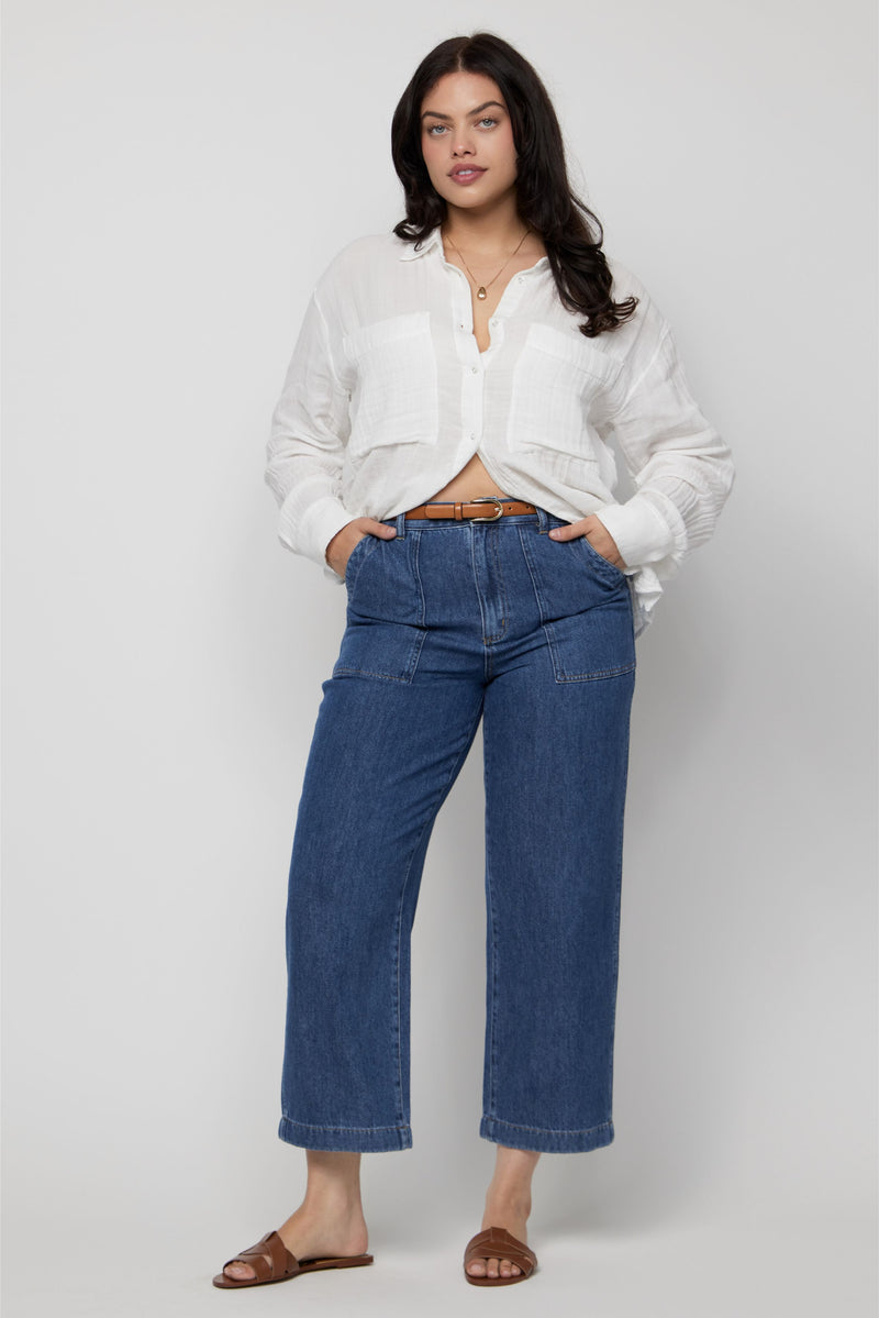 Plus-size model wearing high-rise cropped denim trousers in medium blue wash, styled with a white linen shirt.