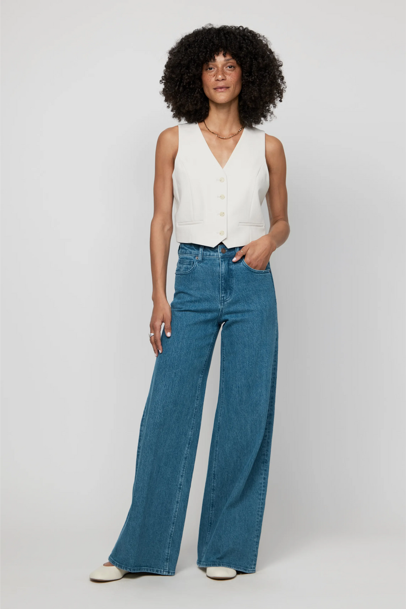 Model in high-rise wide-leg jeans in classic medium blue wash, styled with a cream vest for a polished denim look.