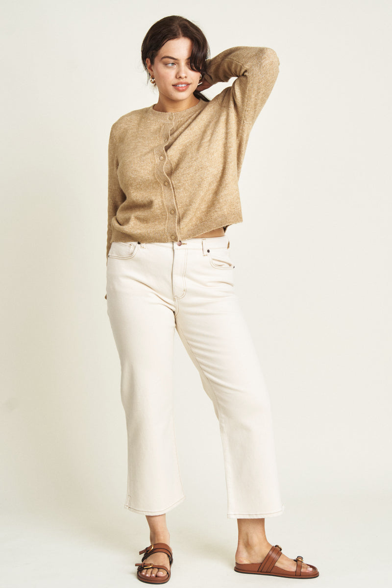 Plus-size model wearing wide-leg ankle crop jeans in an ecru wash, styled with a cream ribbed cardigan and black loafers, showcasing a relaxed fit and cropped hem.