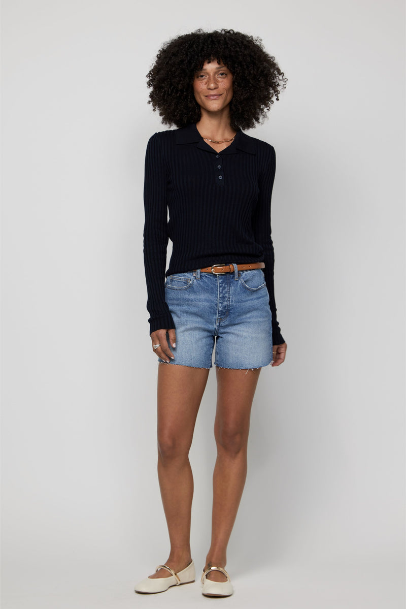Model wearing high-rise denim shorts for women in a light vintage wash, styled with a black ribbed sweater.