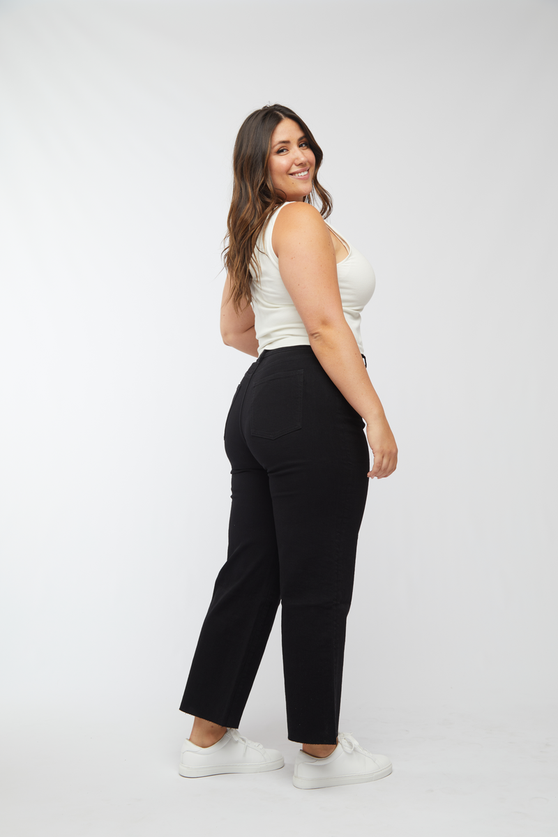 Back view of plus-size model in black wash wide leg cropped jeans, styled with a white top and sneakers, showcasing the high-rise fit.