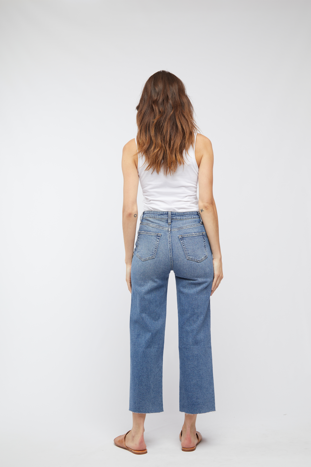 Back view of model in light wash cropped wide leg jeans, paired with brown sandals, highlighting the high-rise design.