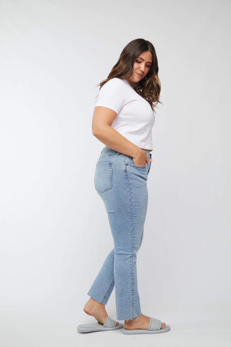 Side profile of plus-size model in light wash high rise jeans, styled with a casual white top, showing off the comfortable, vintage-inspired fit.