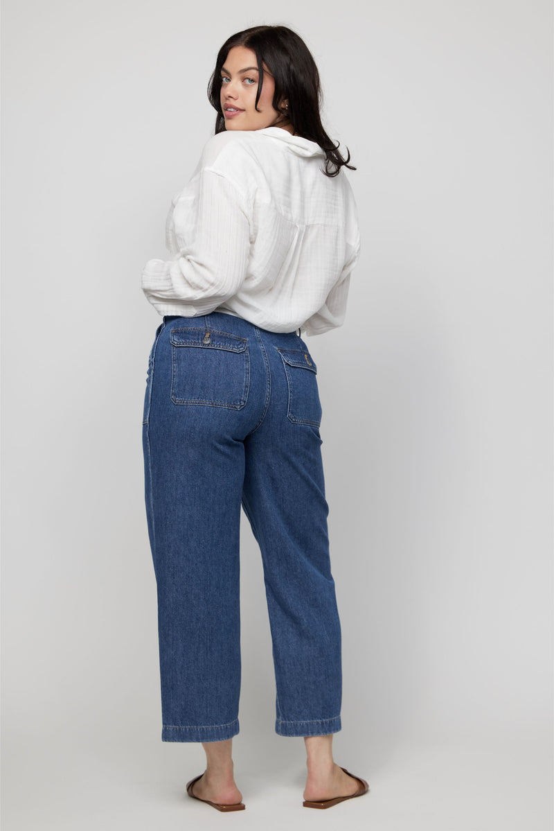 Rear view of plus-size high-rise cropped denim pants in medium indigo wash, styled with sandals.