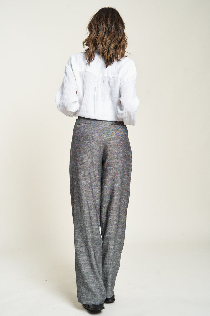 Woman showing the back of high-waisted trousers. Comfortable pleated pants made from breathable cotton, perfect for all-day wear.