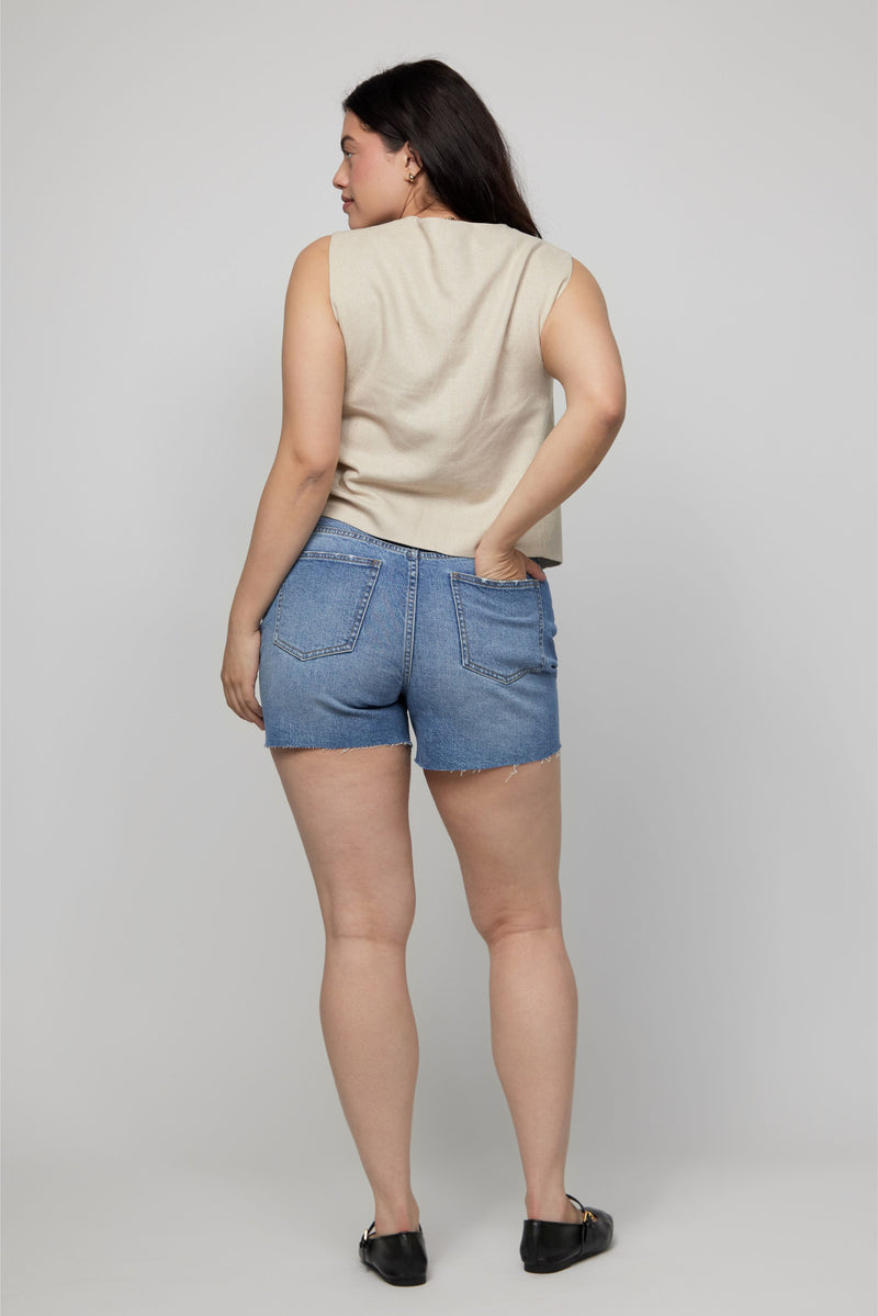 Back view of high-rise denim shorts for plus-size women styled with a sleeveless vest.