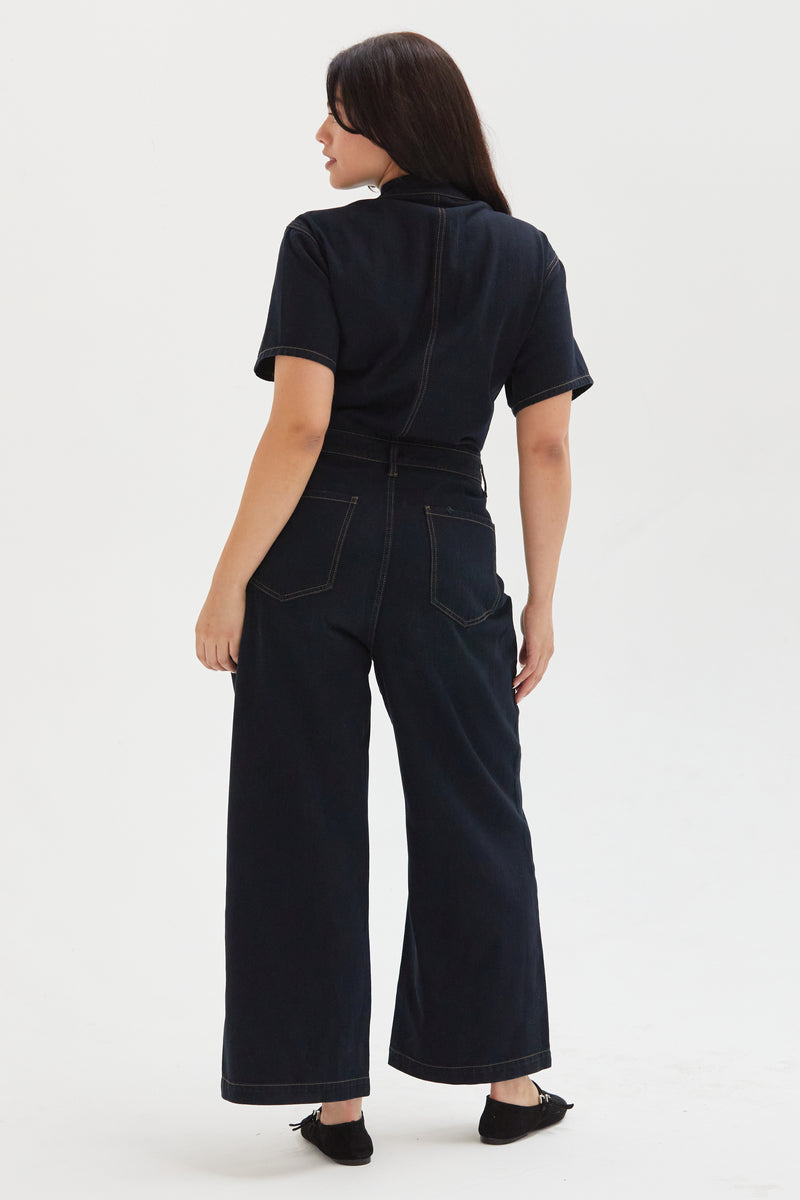 Back view of a plus-size model in a dark indigo romper, highlighting the structured seams and functional design details.