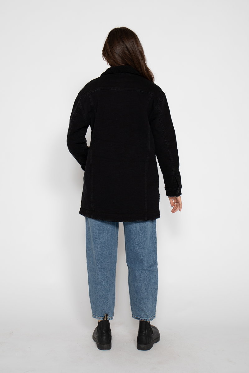 Back view of the black coat, showing its length and relaxed fit over the model&