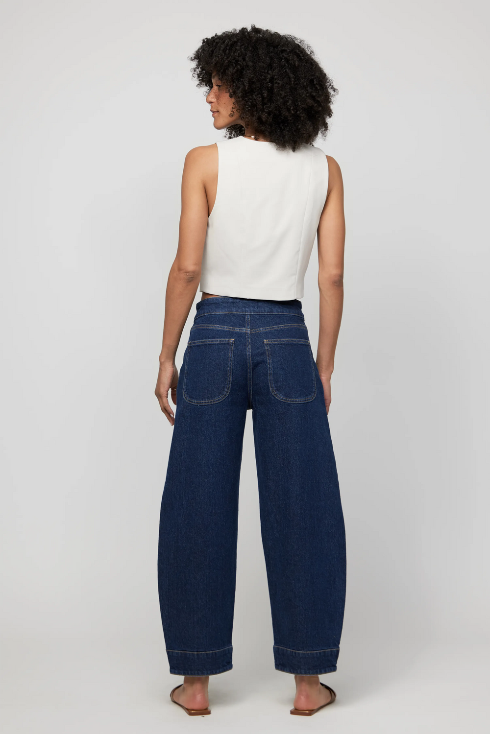 Back view of high-rise barrel-leg jeans in rich dark wash denim, showcasing curved leg fit and clean finish.