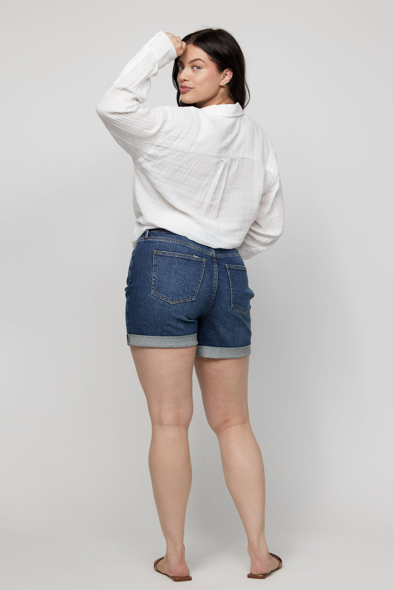 Back view of high-rise denim shorts for women in a dark wash, styled with a relaxed white blouse.