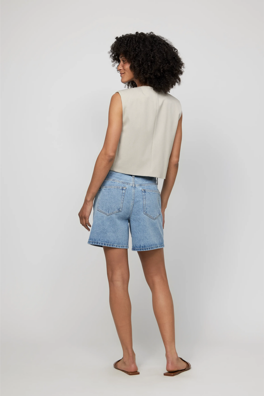 Back view of light wash high-rise jean shorts paired with a neutral sleeveless top and flats.