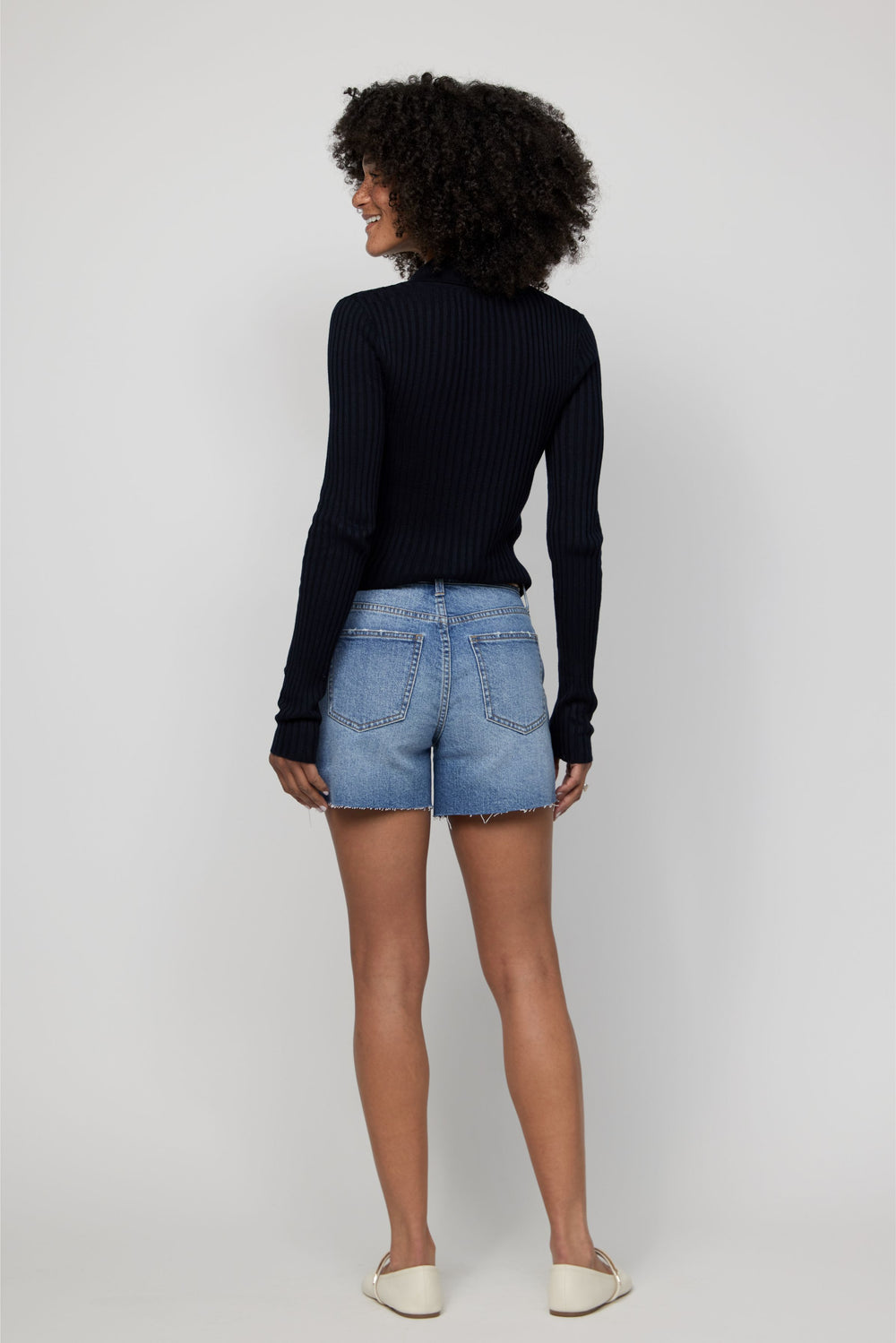 Back view of high-rise denim shorts for women in a faded light blue wash paired with a black top.