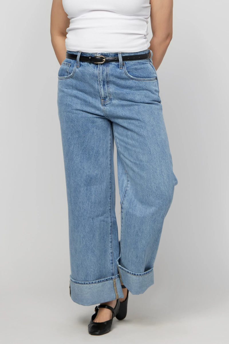 Front close-up of mid-rise light wash wide-leg jeans with deep cuffs on plus-size model.