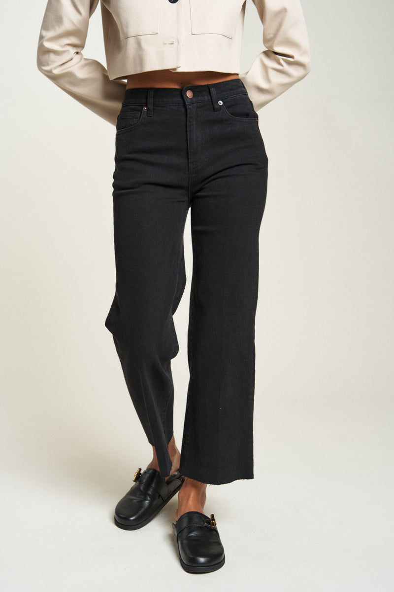 Close-up of black wash high waisted cropped wide leg jeans, paired with a beige jacket, highlighting the clean silhouette.