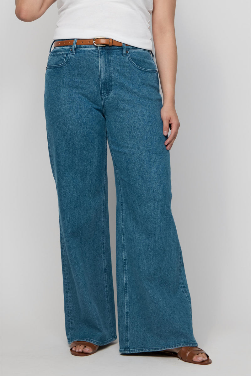 Close-up of high-rise wide-leg jeans in medium blue wash on plus-size model, featuring structured fit and soft denim texture.