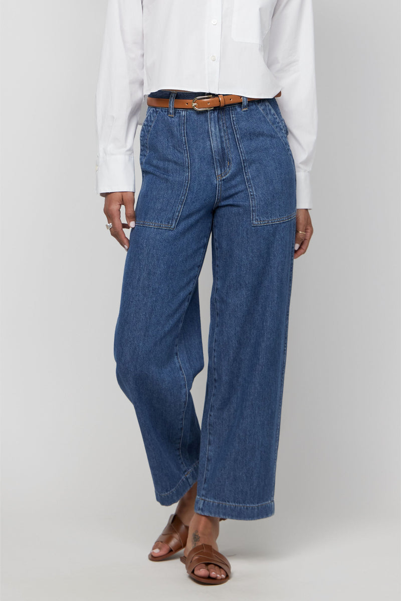 Close-up of medium blue high-rise wide-leg denim trousers with front seam detail and relaxed fit.