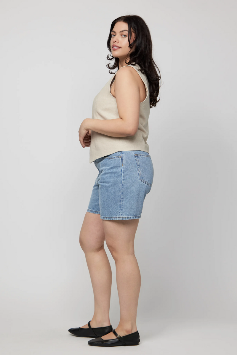 Side view of high-rise light wash denim shorts on plus-size woman with sleeveless blouse.