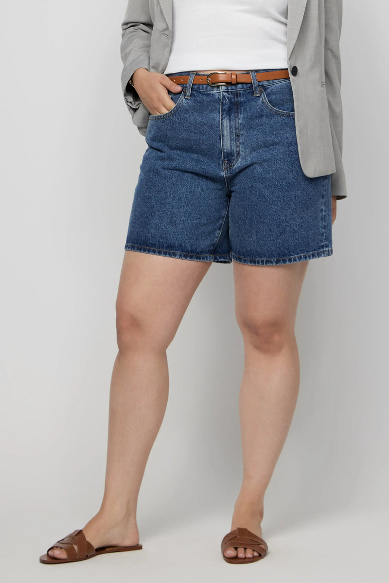 Close-up of high-rise dark denim shorts for plus-size women, styled with a belt and grey blazer.