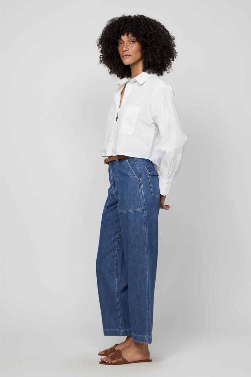 Side angle of woman in high-rise wide-leg cropped trousers in medium blue, styled with flat sandals.