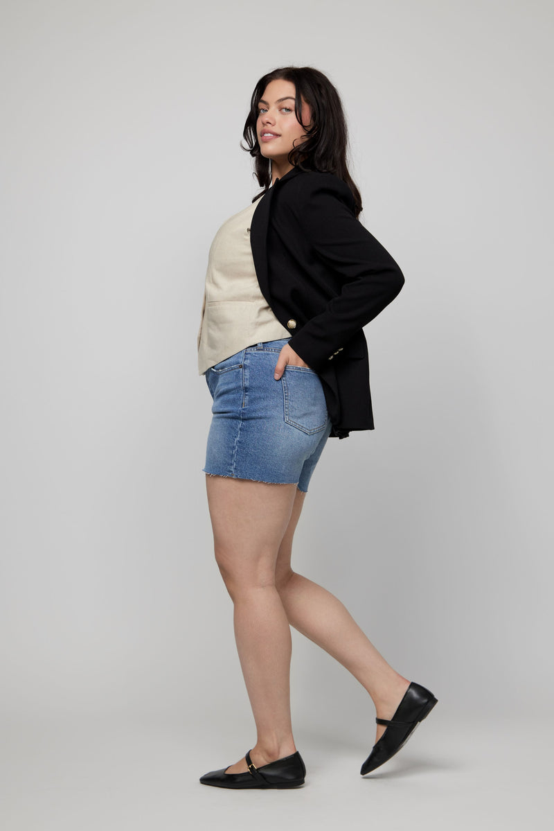 Side view of plus-size high-rise denim shorts styled with a vest and flats for an elevated casual outfit.
