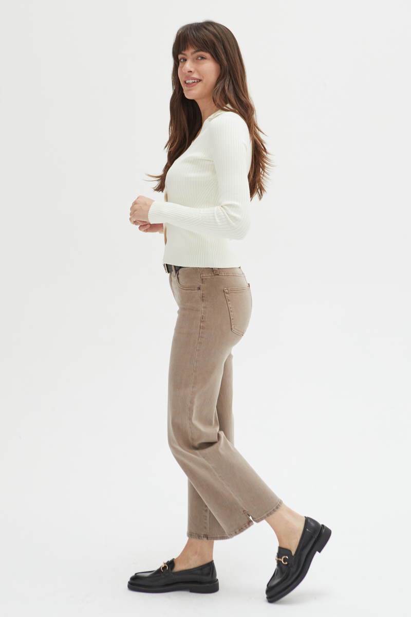 Side view of a model in brown wide-leg ankle crop jeans, paired with a black belt and cream top, showcasing their versatility and timeless style.