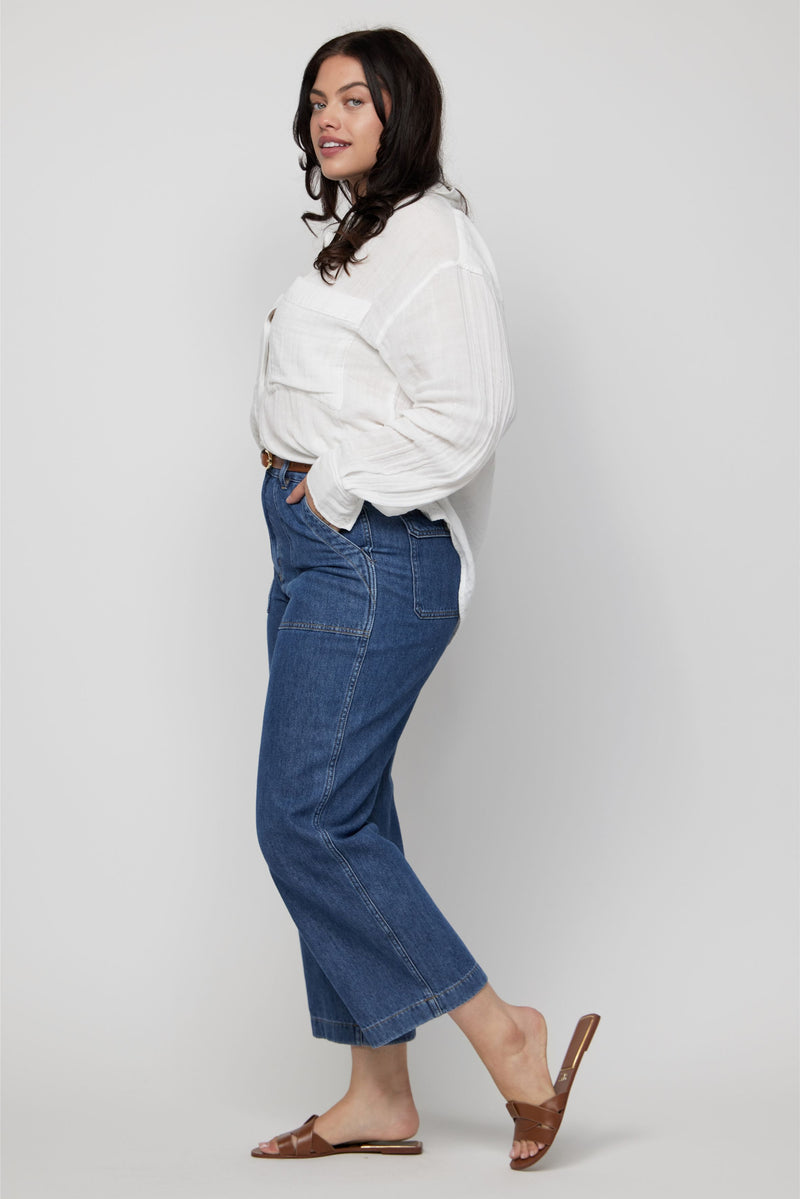 Side profile of plus-size woman in high-rise cropped jeans in medium blue wash with a casual white top.