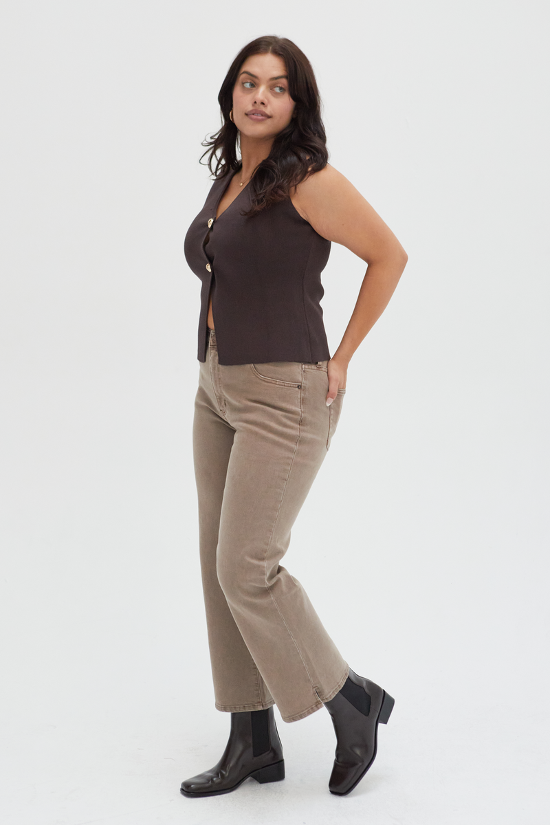 Side view of a plus-size model in brown wide-leg ankle crop jeans, paired with a black belt and cream top, showcasing their versatility and timeless style.
