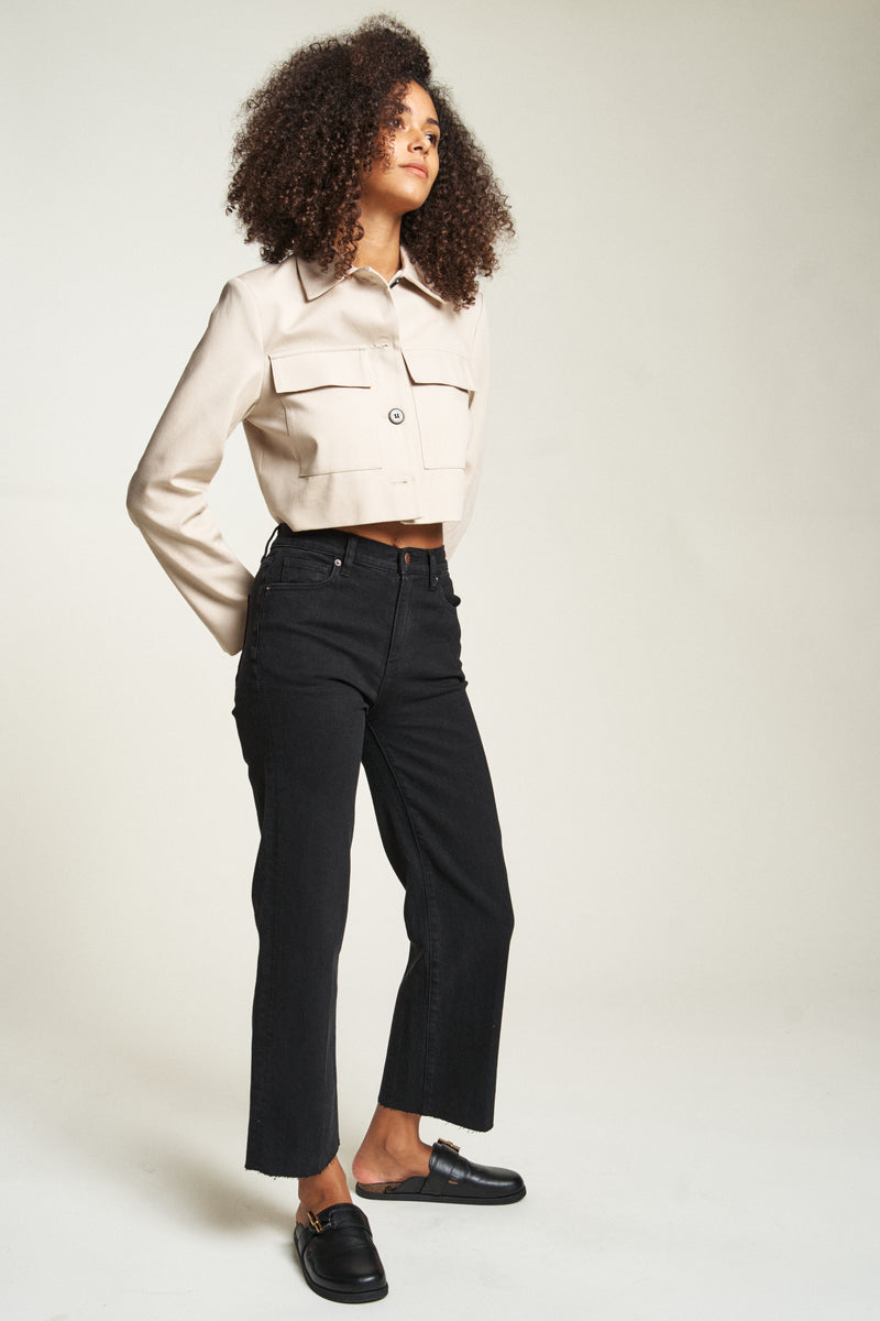 Model posing confidently in black wash wide leg jeans, styled with black shoes and a beige jacket, side view.