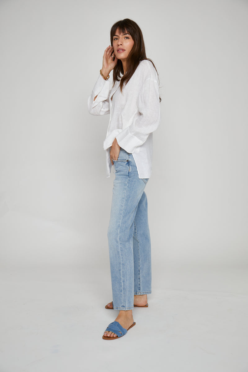 Side view of model confidently posing in light washed straight leg jeans, paired with sandals, emphasizing the timeless light denim look.