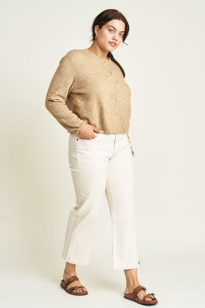 Side view of a plus-size model in ecru wide-leg ankle crop jeans, paired with a black belt and cream top, showcasing their versatility and modern appeal.