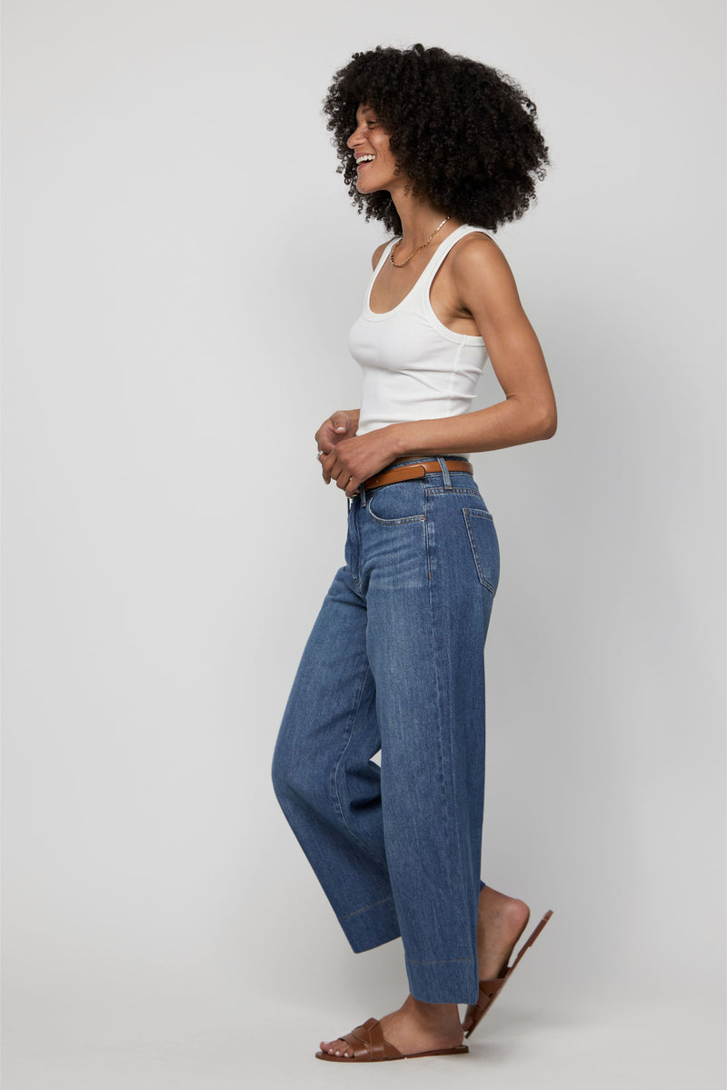Side angle of high-rise plus-size wide-leg cropped denim pants styled with a white tank and flats.