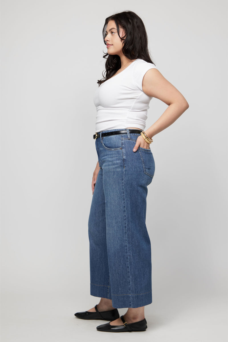 Angled view of woman modeling high-rise cropped wide-leg denim in medium indigo with relaxed fit.