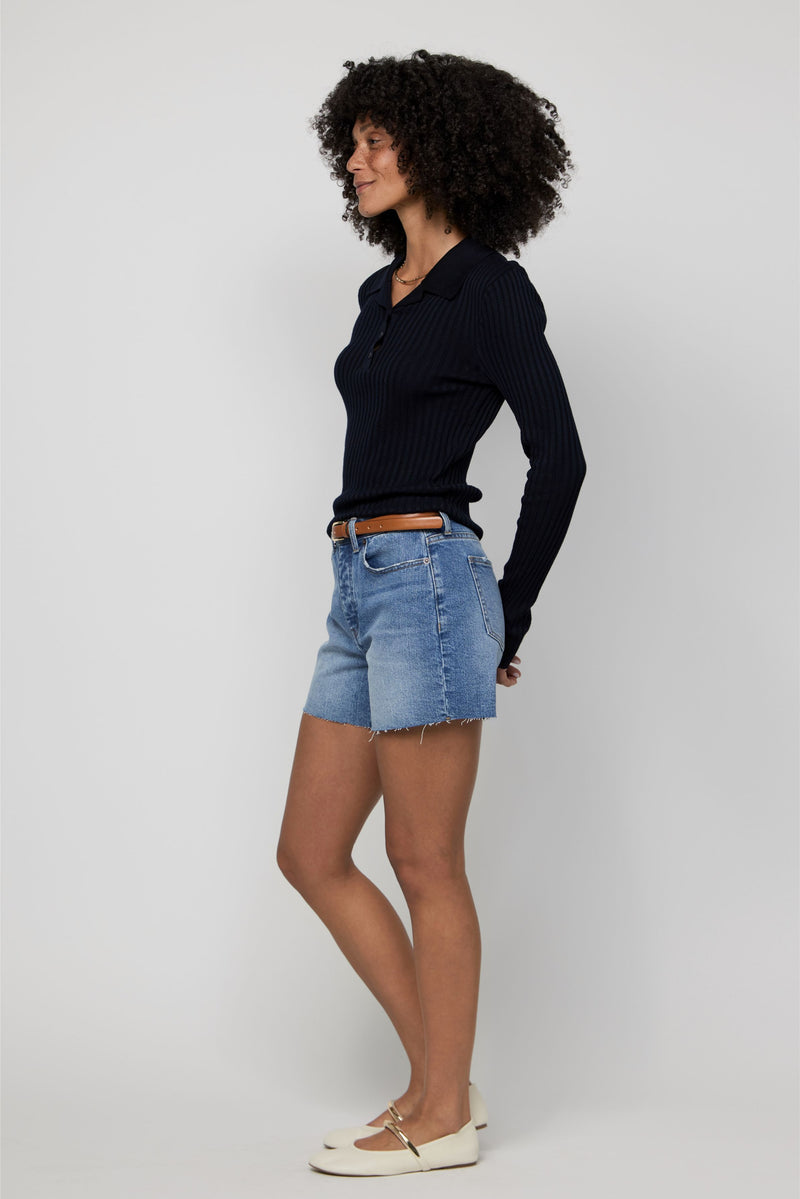 Side view of high-rise denim shorts for women paired with a sweater and flats for a polished, casual outfit.