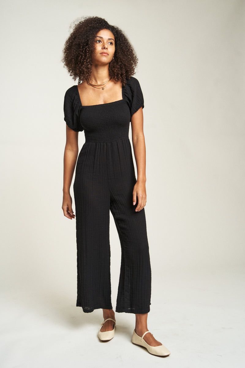 Flowy black romper crafted from lightweight cotton, featuring a square neckline and loose-fitting legs for easy movement.