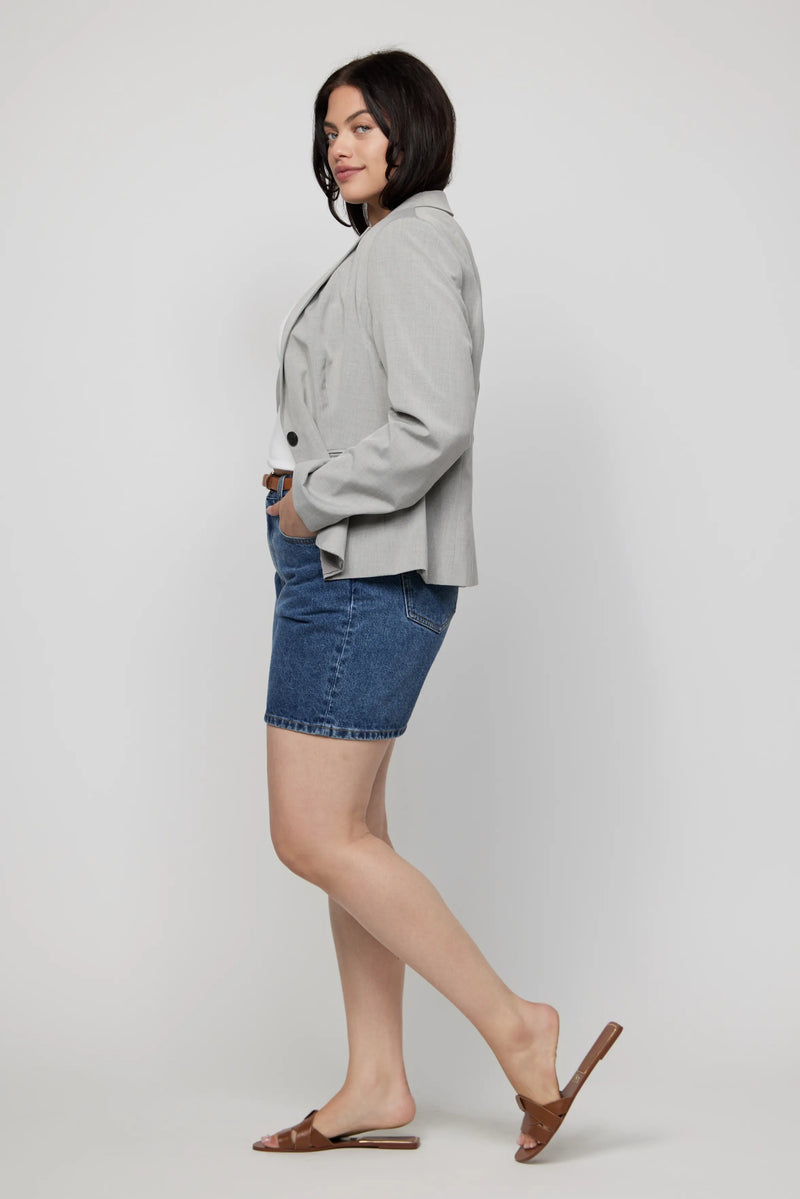 Side view of plus-size high-rise jean shorts paired with a relaxed blazer and slip-on sandals.