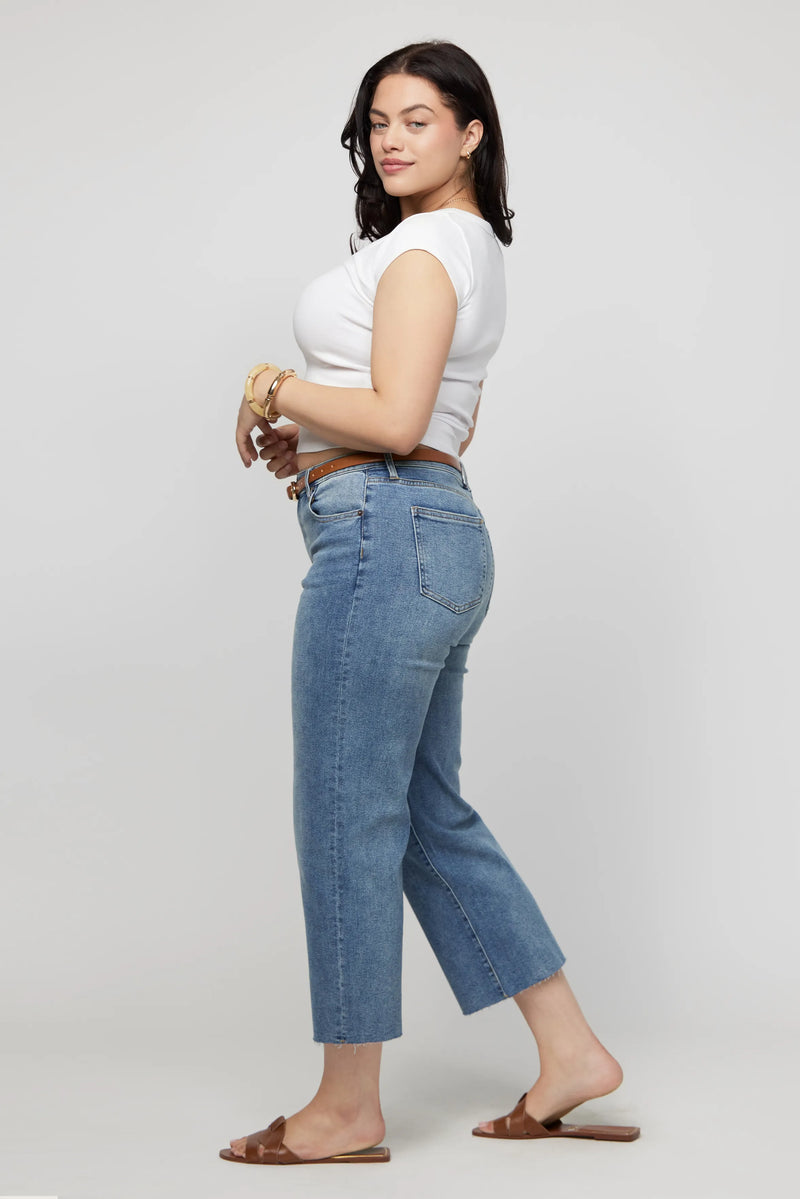 Side view of a woman in plus-size cropped jeans, paired with a white tank and minimal sandals for a clean, modern look.